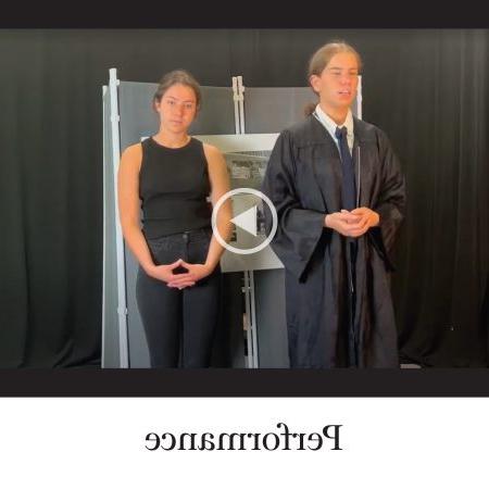 Labeled ‘Performance.两名学生肩并肩站在一起的视频剧照. 一个系着领带，穿着黑袍，另一个一身黑.
